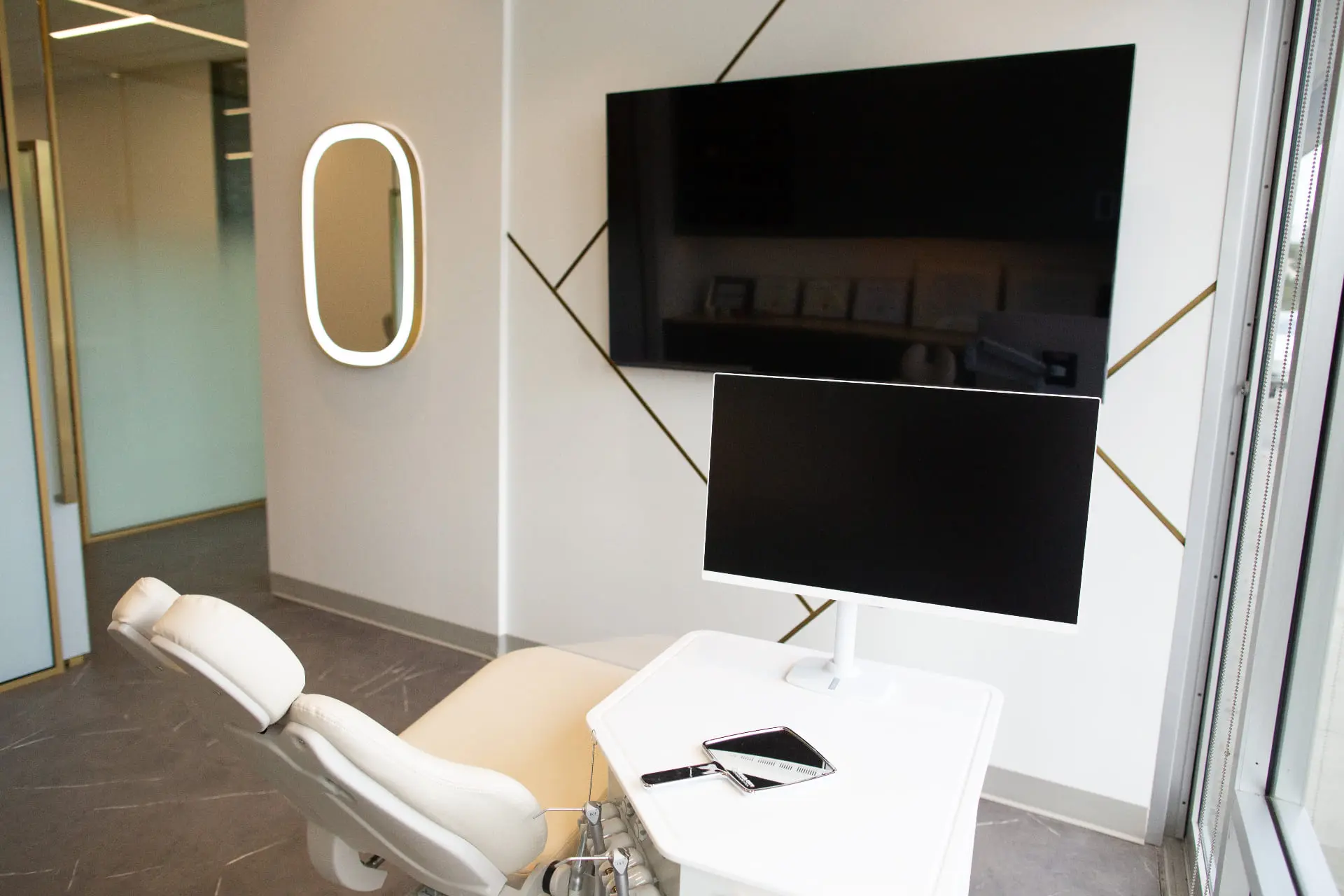 A sleek dental office at Emerald City Orthodontics in Kirkland WA, with a white chair, monitor, smartphone, and wall-mounted TV.