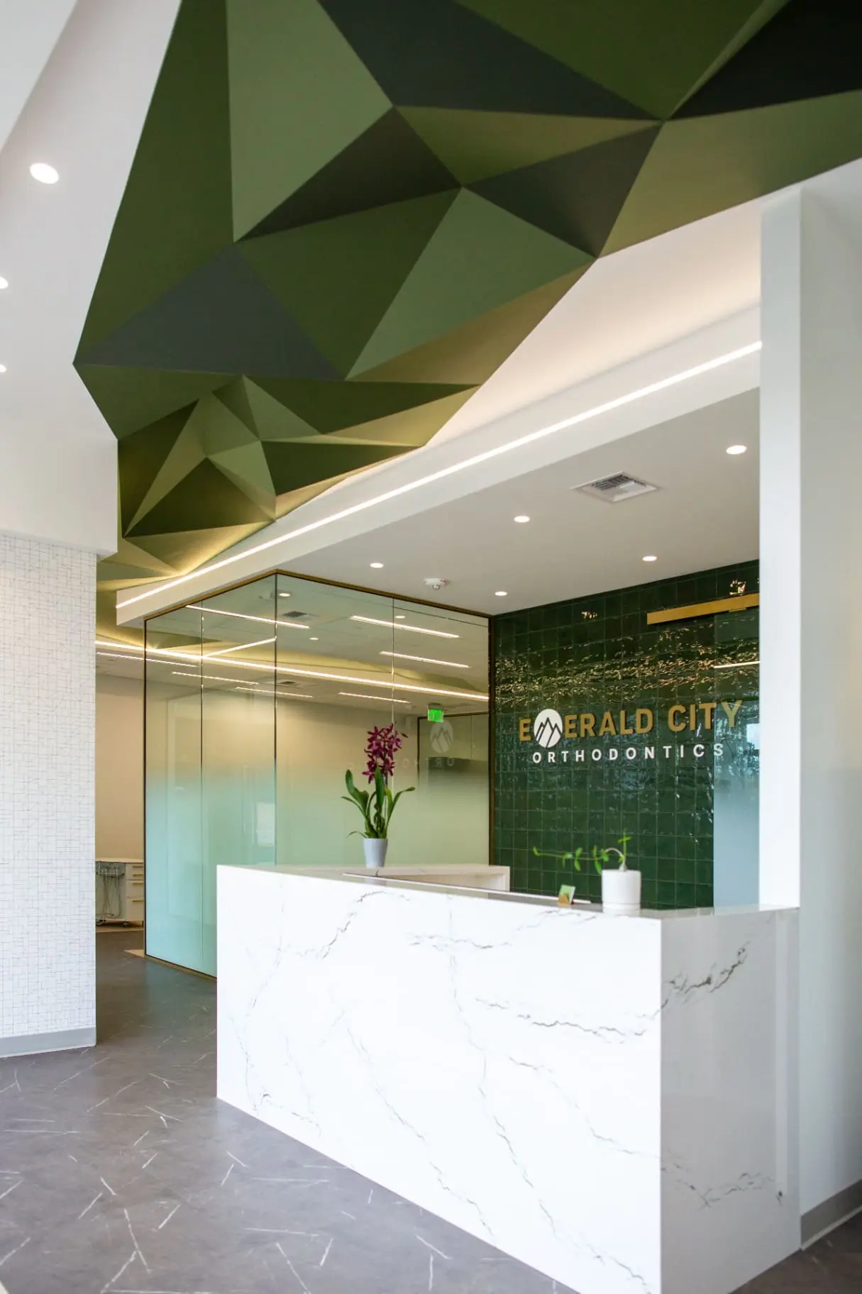 The lobby at Emerald City Orthodontics in Kirkland, WA features a marble reception desk, green geometric ceiling, and tiled wall.