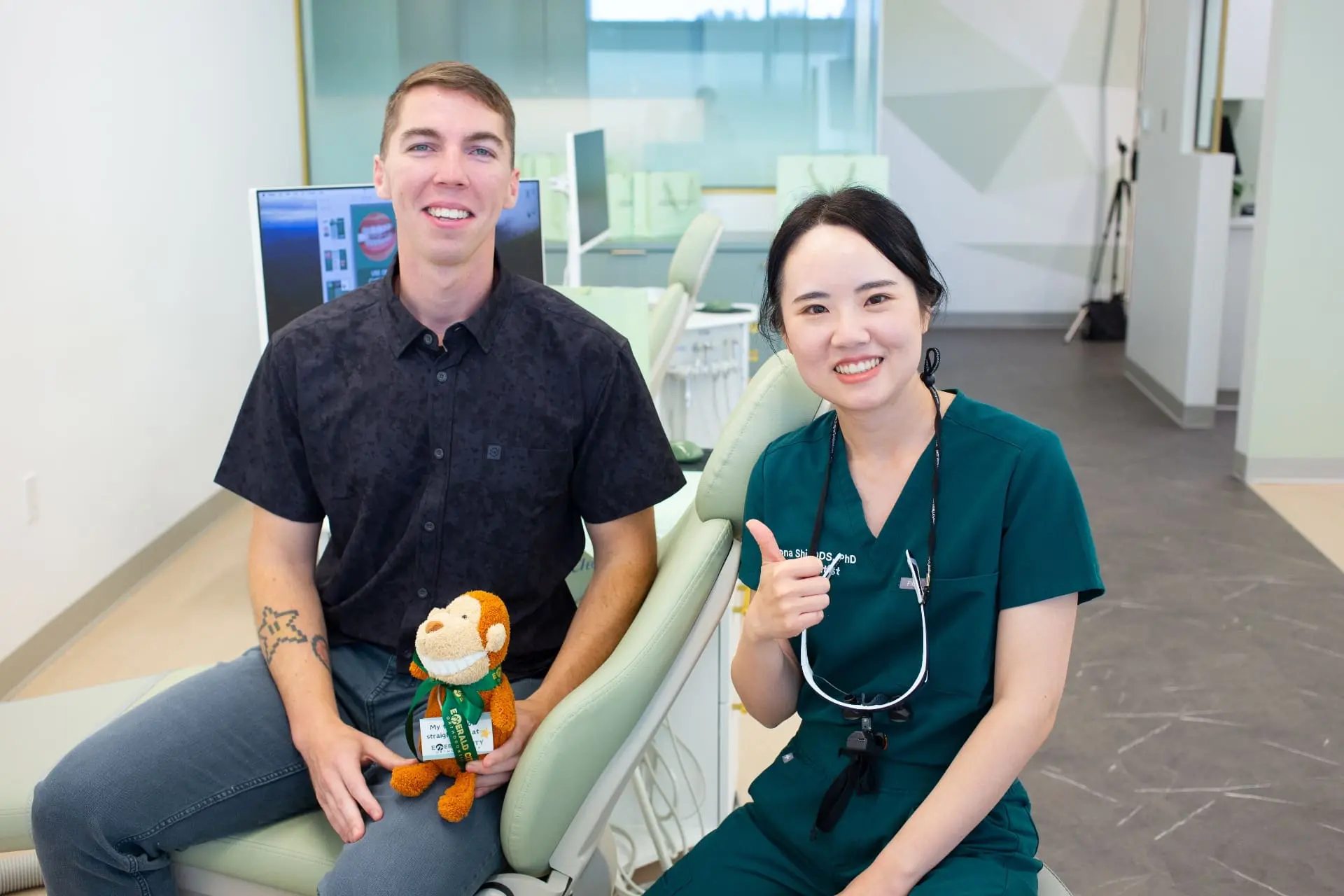 At Emerald City Orthodontics in Kirkland WA, a man with a stuffed animal sits beside a smiling dental professional giving a thumbs-up.