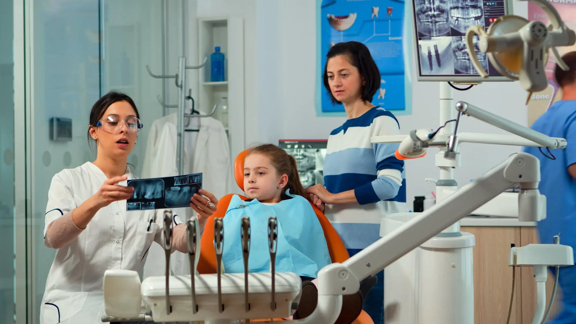 A children's orthodontist at Emerald City Orthodontics in Kirkland, WA shows a dental X-ray to a girl and her mother.