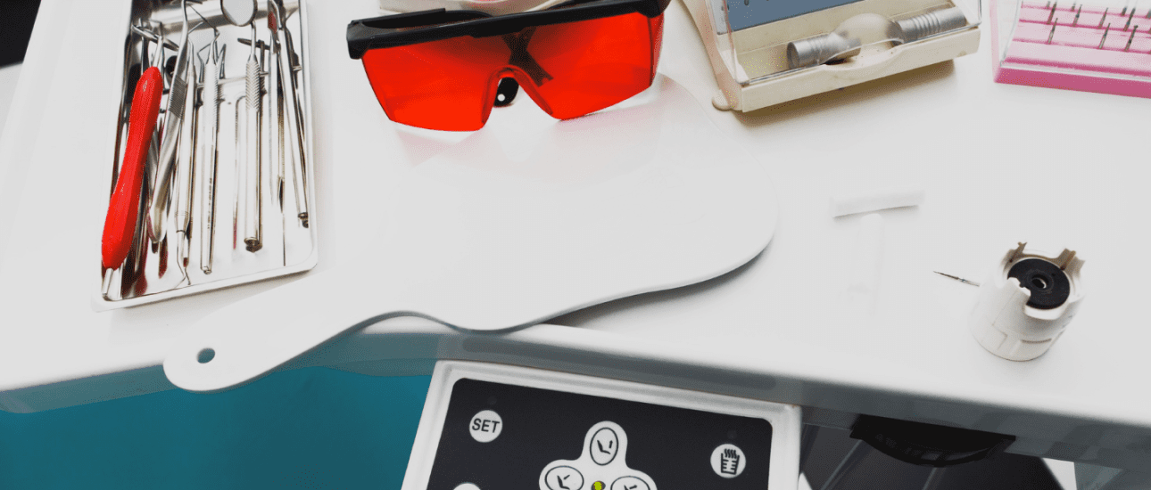 On a white surface at Emerald City Orthodontics in Kirkland, WA: dental tray with metal braces tools, red glasses, mirror, control panel.