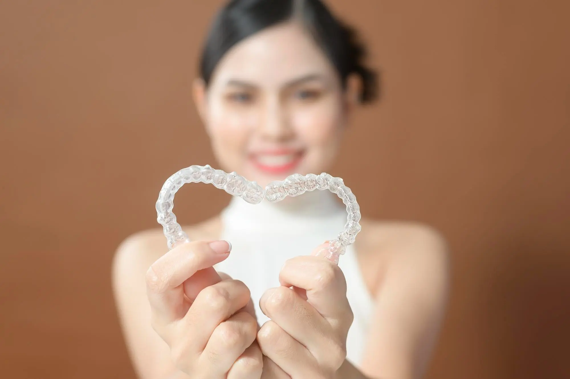 At Emerald City Orthodontics in Kirkland WA, a person shapes two clear aligners into a heart, symbolizing Invisalign vs braces.