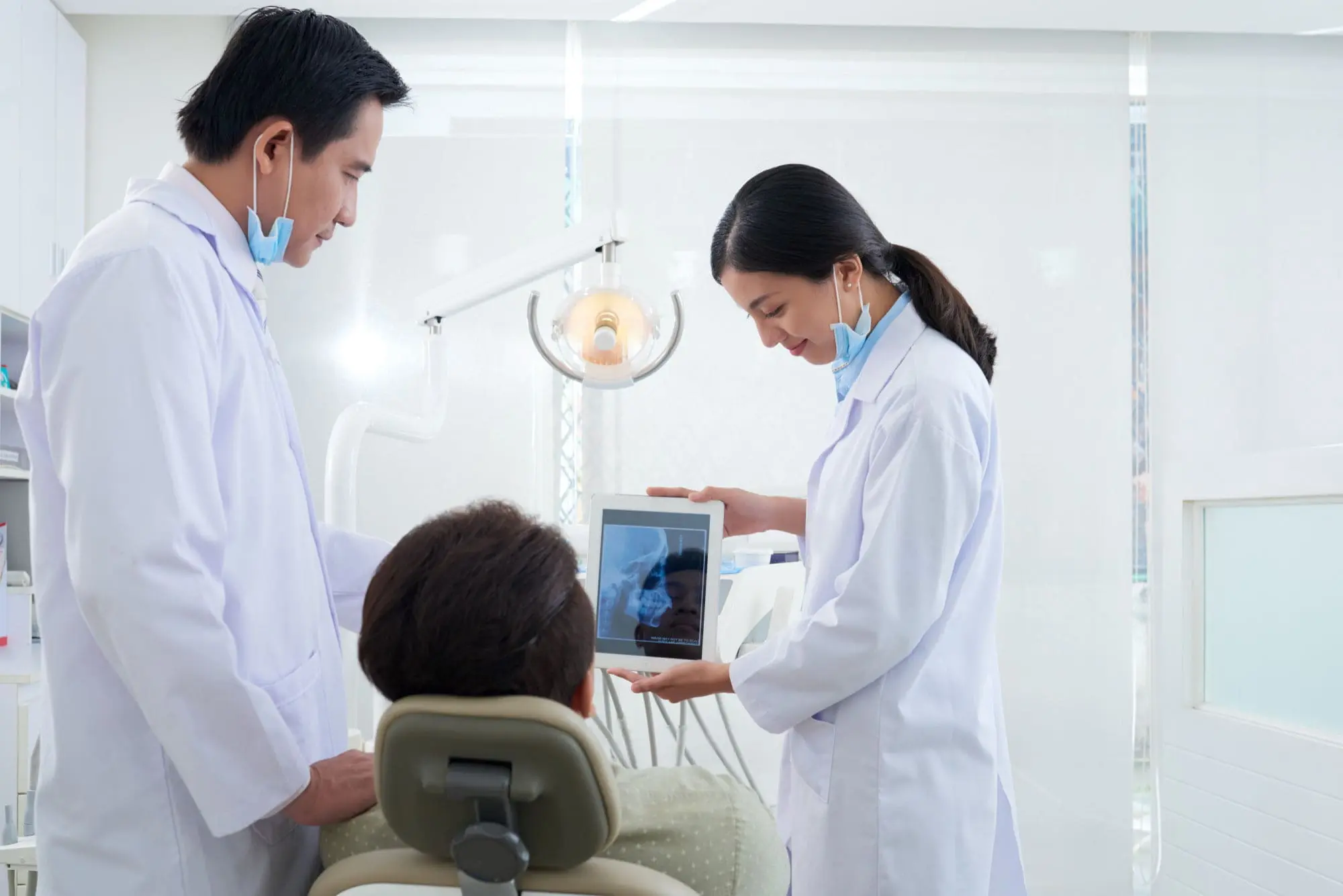 Dentists at Emerald City Orthodontics in Kirkland, WA show a dental X-ray on a tablet to a patient, discussing jaw surgery.
