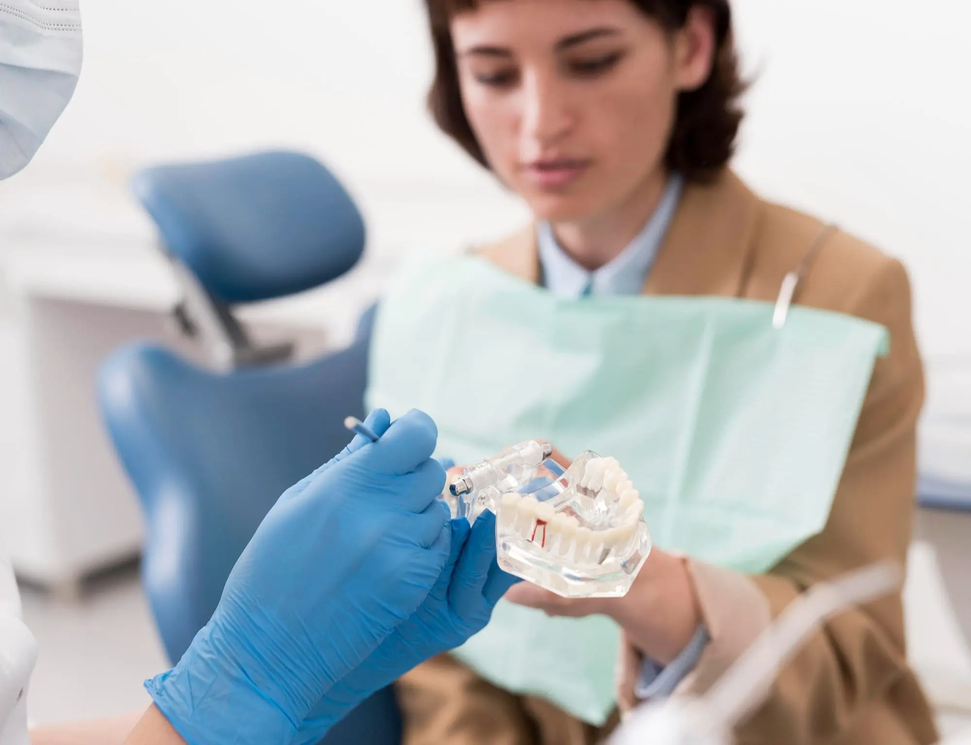 A dentist in blue gloves at Emerald City Orthodontics in Kirkland, WA explains jaw surgery using a teeth model to a patient.