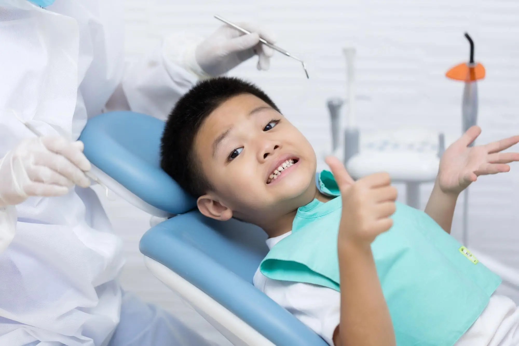 At Emerald City Orthodontics in Kirkland WA, a child gives a thumbs up in the dental chair as an orthodontist holds dental tools.