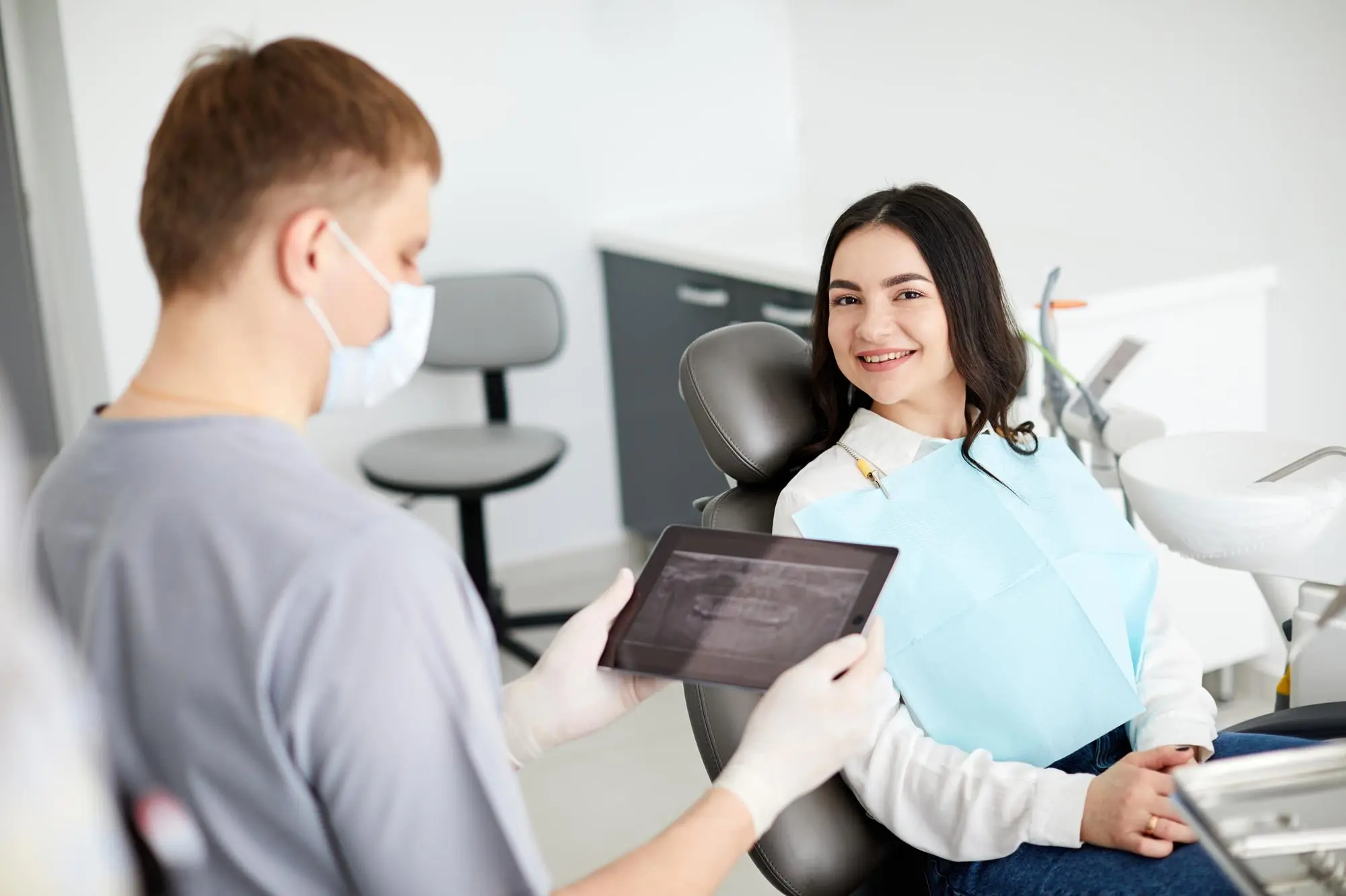 A dentist shows a dental X-ray on a tablet to a smiling patient with metal braces at Emerald City Orthodontics in Kirkland, WA.