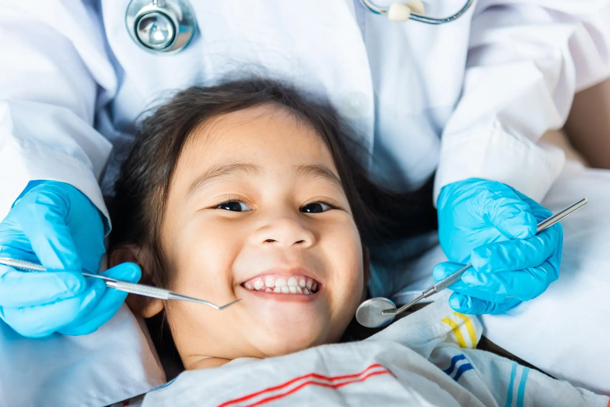 A smiling child at a dental checkup with a gloved dentist; expert care by Emerald City Orthodontics in Kirkland, WA.