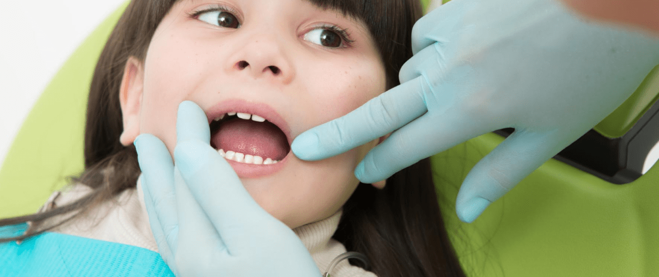 At Emerald City Orthodontics in Kirkland WA, a child in a dental chair has their teeth examined by an orthodontist in blue gloves.