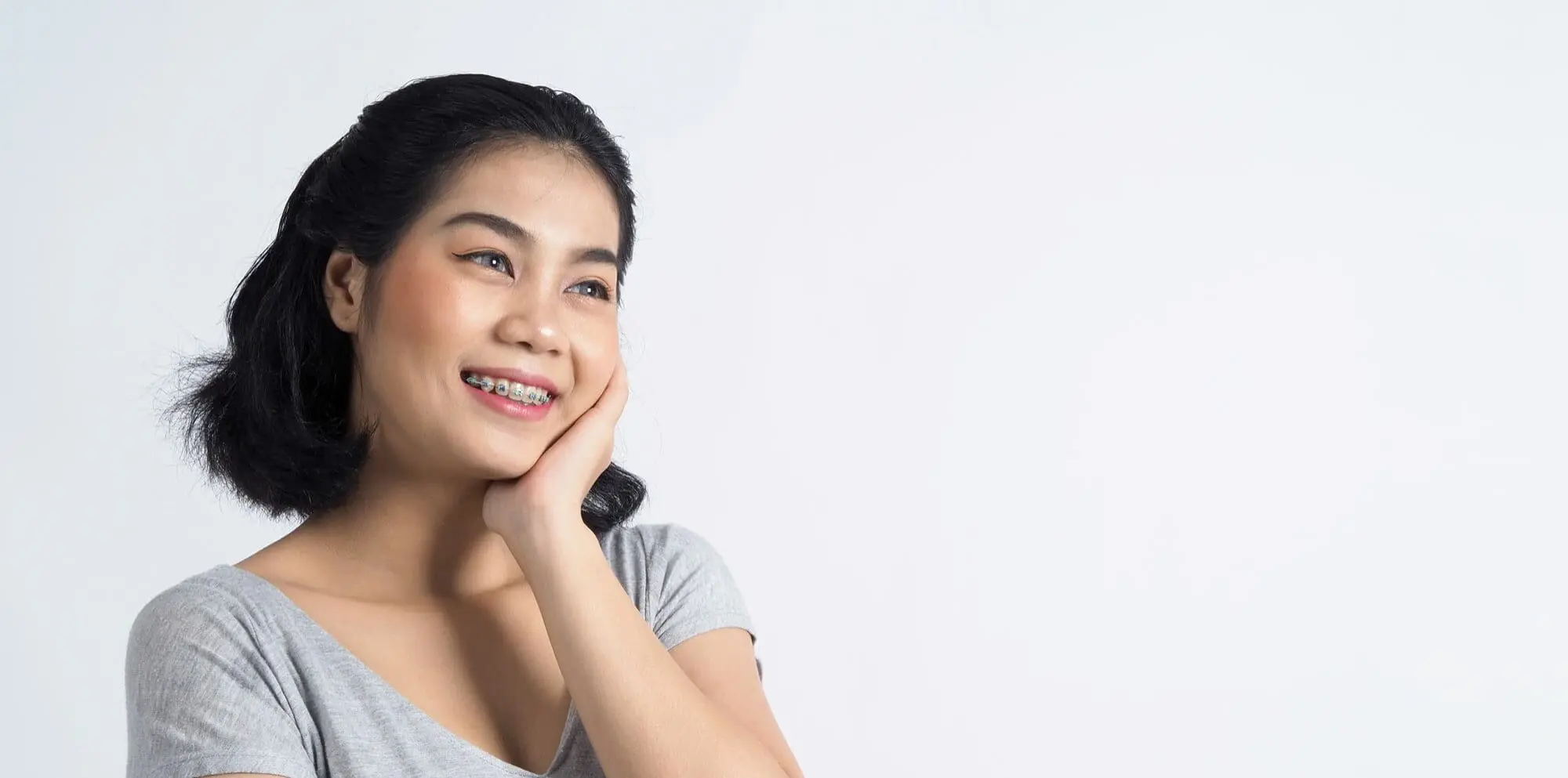 Smiling with braces, a person highlights adult orthodontics at Emerald City Orthodontics in Kirkland WA, on white background.