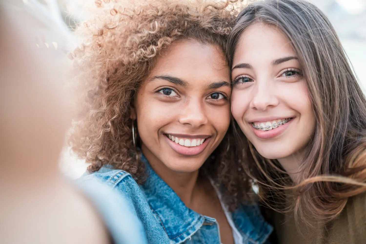 Smiling outdoors, two young women—one with braces, represent free orthodontic consultation for Braces available at Emerald City Orthodontics in Kirkland, WA.