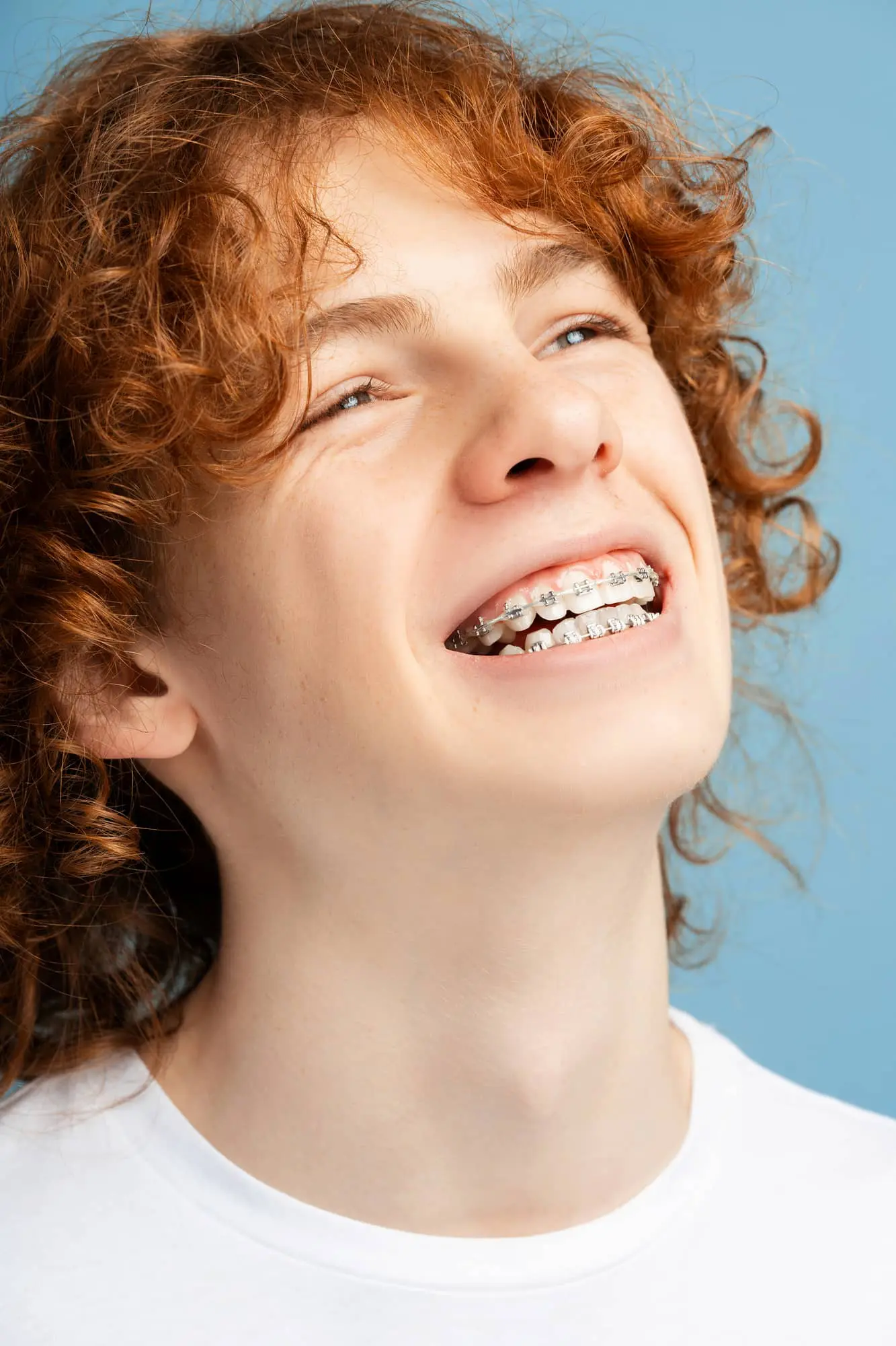 Smiling red-haired teen shows metal braces, highlighting care for all ages at Emerald City Orthodontics in Kirkland, WA.