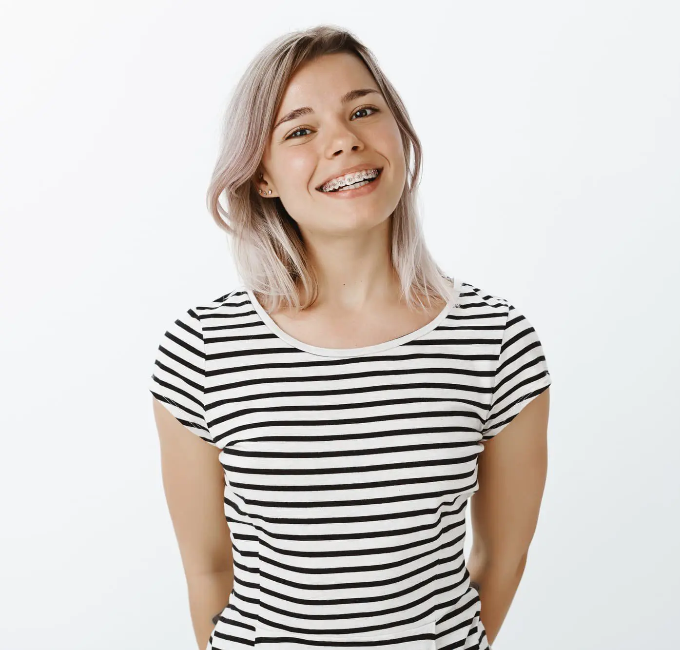 Smiling young woman with braces for fix Overbite at Emerald City Orthodontics in Kirkland, WA, in a striped shirt against a white background.