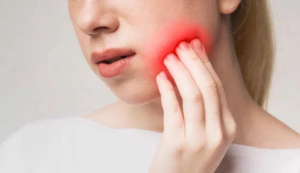 A woman touches her cheek, red with pain—an issue Emerald City Orthodontics in Kirkland, WA sees with Invisalign vs braces.
