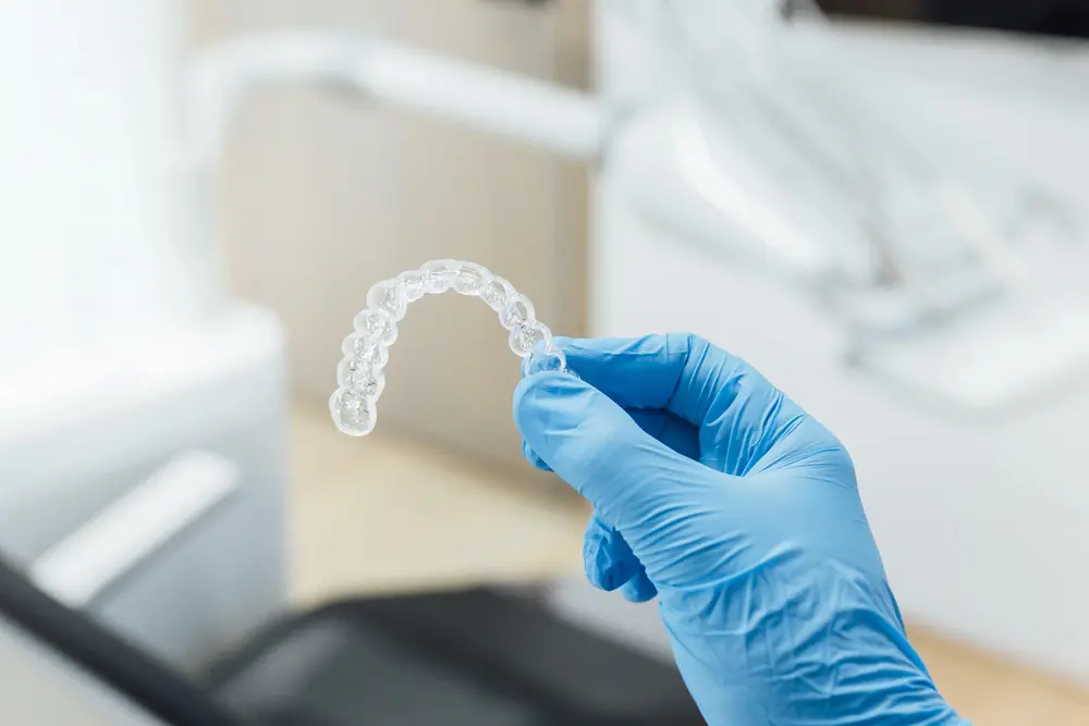 A gloved hand holds a clear aligner at Emerald City Orthodontics in Kirkland WA, showcasing Invisalign Payment Plan options.