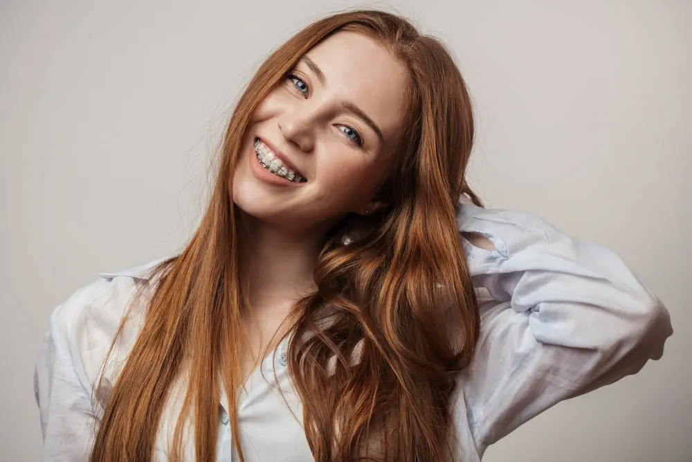 A smiling young woman with red hair and braces shows confidence after adult orthodontics at Emerald City Orthodontics in Kirkland, WA.