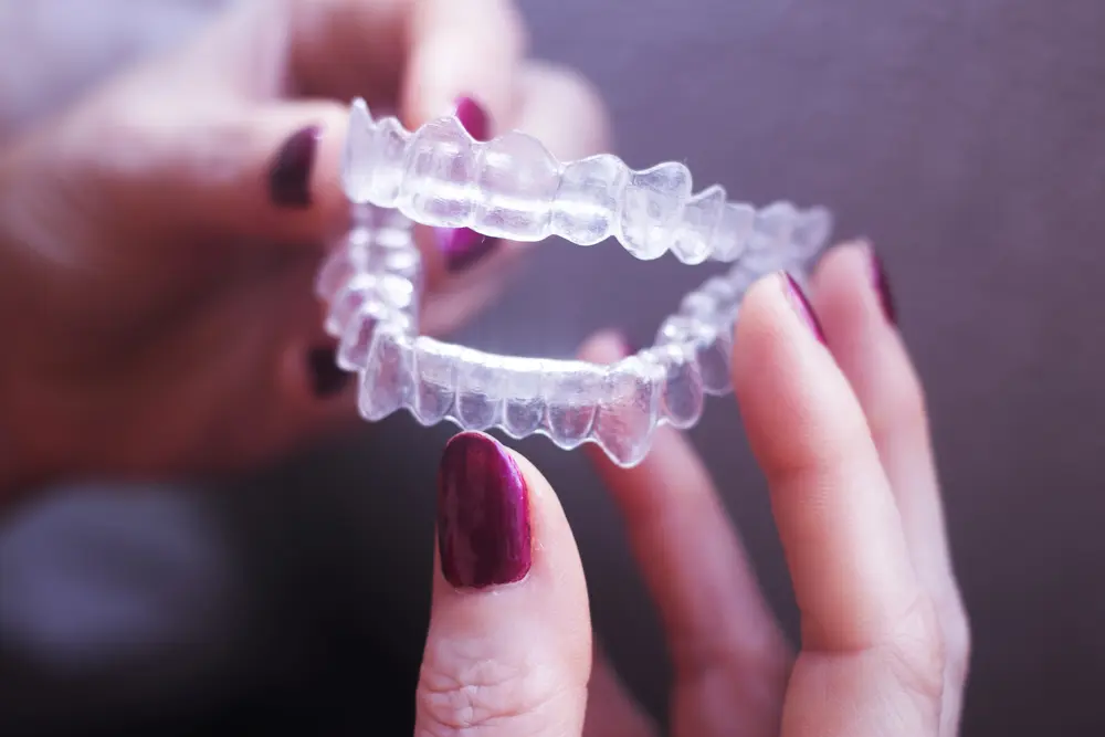 With dark red nails, a person holds dental aligners, considering an Invisalign Payment Plan at Emerald City Orthodontics in Kirkland, WA.