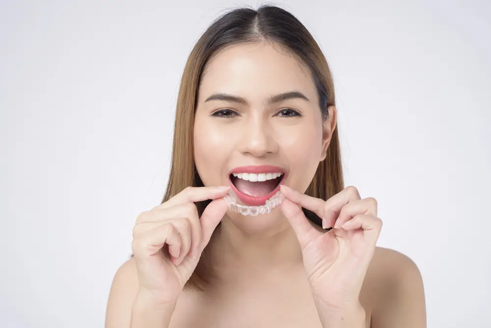Smiling woman holding a clear aligner near her teeth, showing Emerald City Orthodontics in Kirkland, WA offers discreet alternatives.