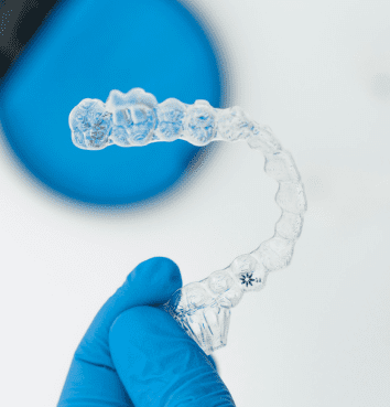 A gloved hand holds a clear aligner, showcasing Invisalign Payment Plan simplicity at Emerald City Orthodontics in Kirkland, WA.