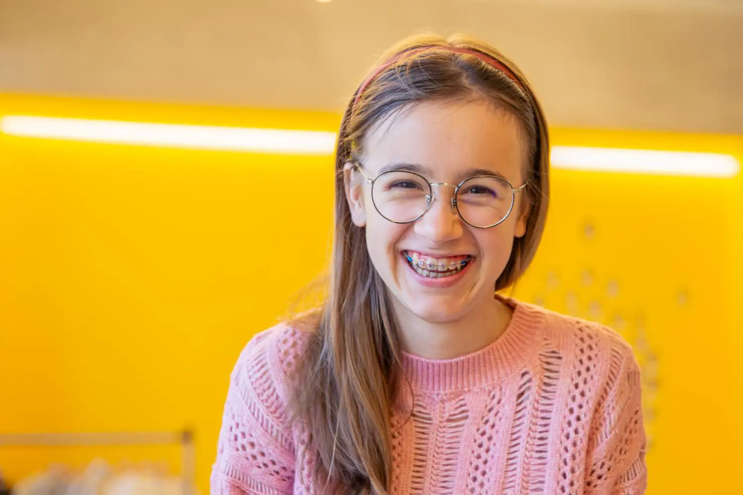 A smiling girl with long brown hair, glasses, and braces represents the age factor in Orthodontics from Emerald City Orthodontics in Kirkland, WA.