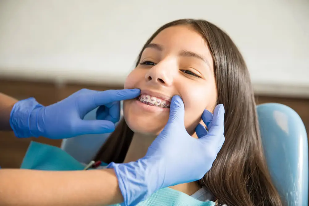 A children's orthodontist at Emerald City Orthodontics in Kirkland, WA checks a smiling girl's braces as she sits in the chair.