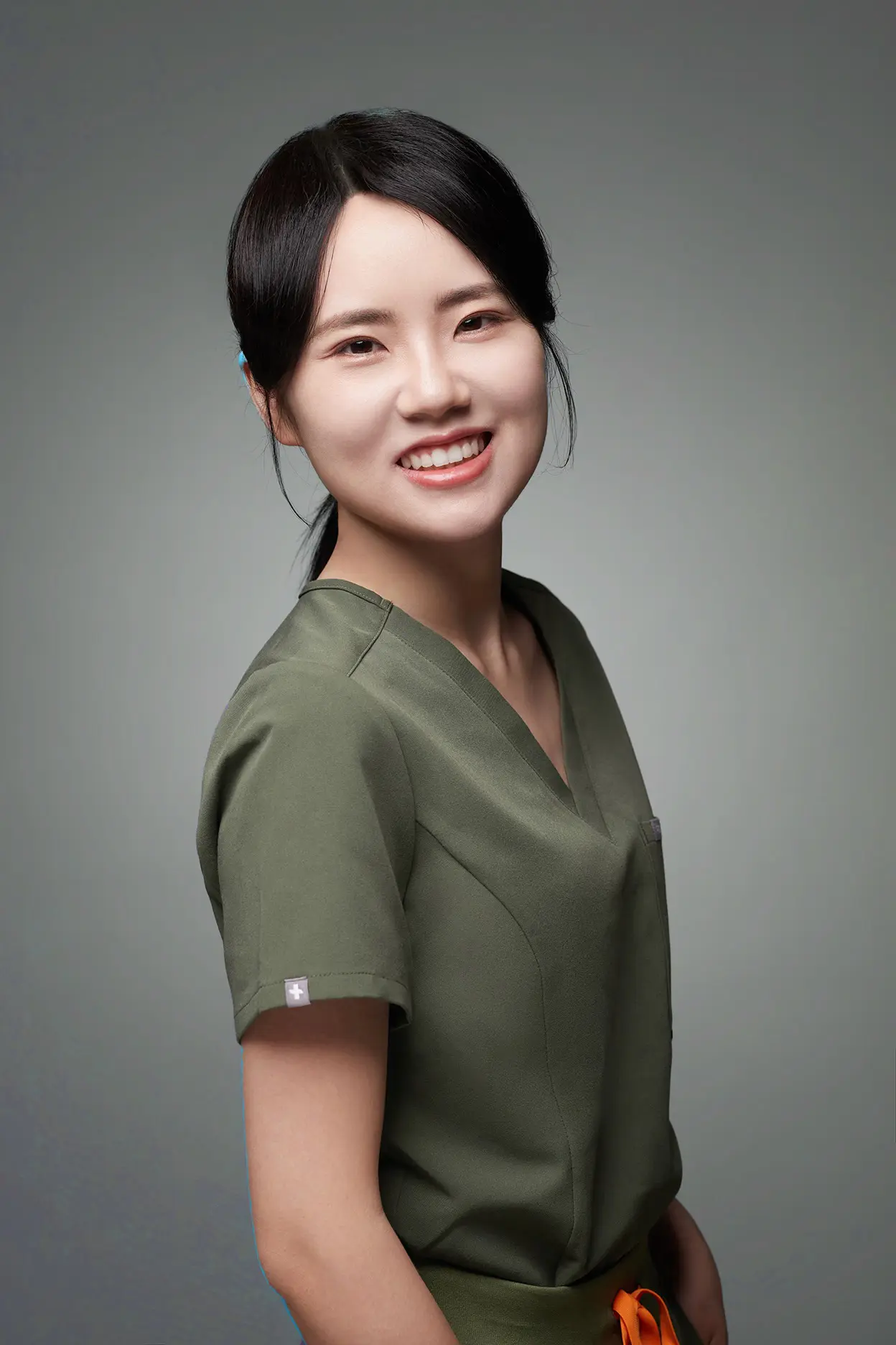 Dr. Jiayu (Fiona) Shi, orthodontist expert at Emerald City Orthodontics in Kirkland WA, smiling confidently in a professional portrait wearing green scrubs against a neutral background.