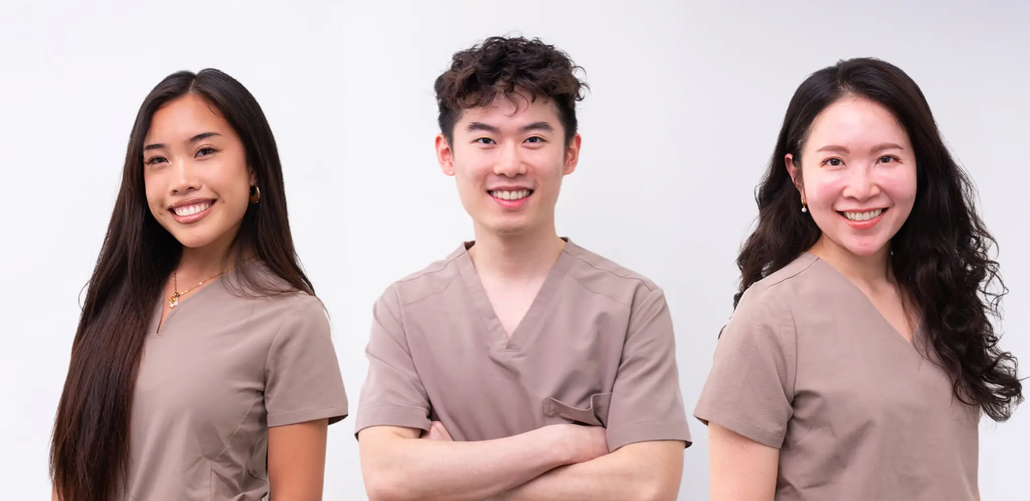 Staff at Emerald City Orthodontics in Kirkland, WA wear beige scrubs and smile side by side against a plain light background.