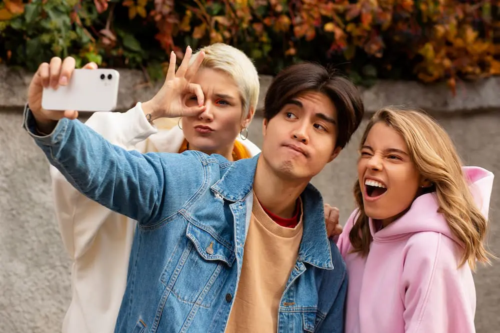 Three teens outside in autumn show off braces from Emerald City Orthodontics in Kirkland, WA while snapping a cheerful selfie.
