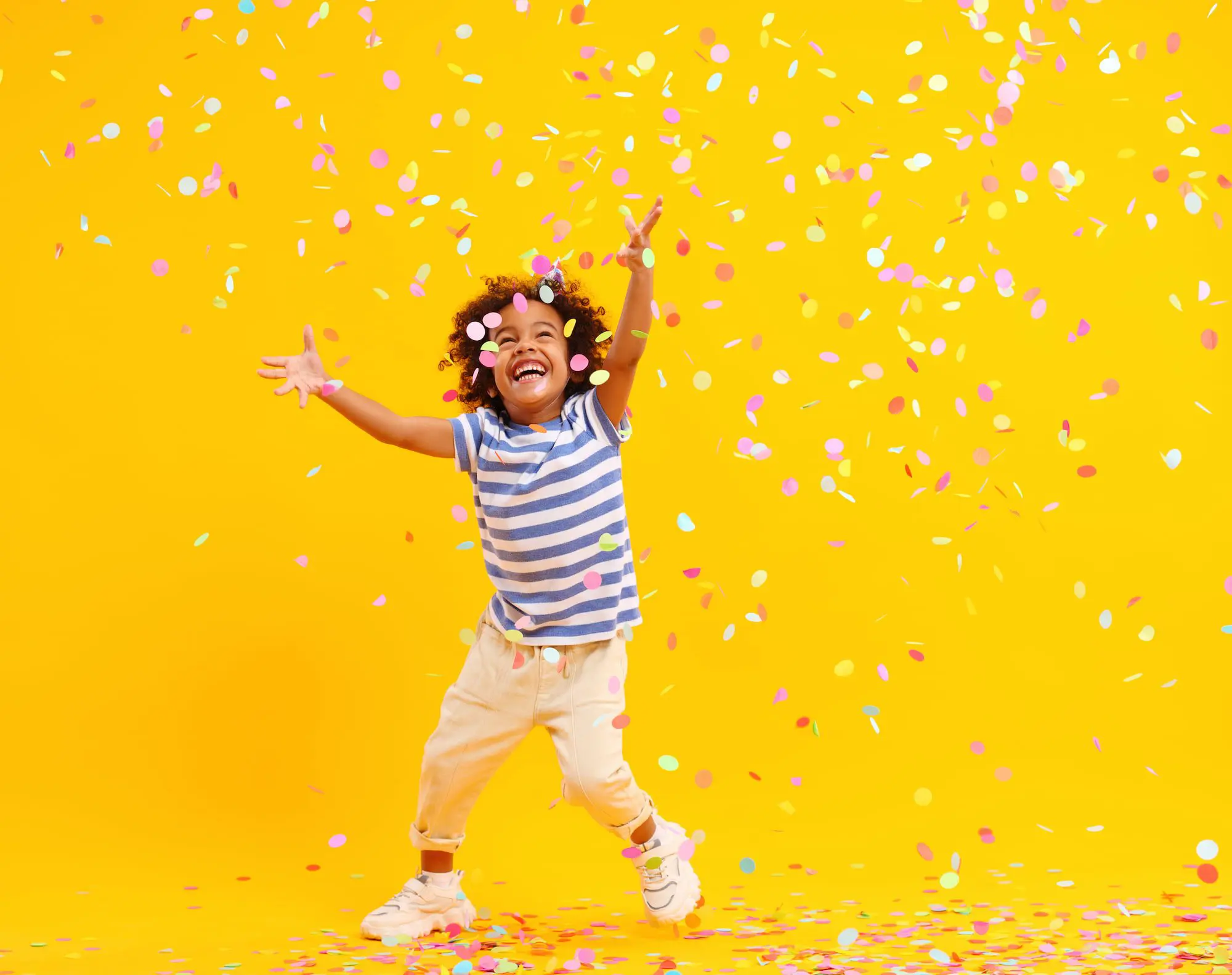 Amid confetti on yellow, a child in striped shirt and light pants with Herbst Appliance smiles; Emerald City Orthodontics in Kirkland, WA.