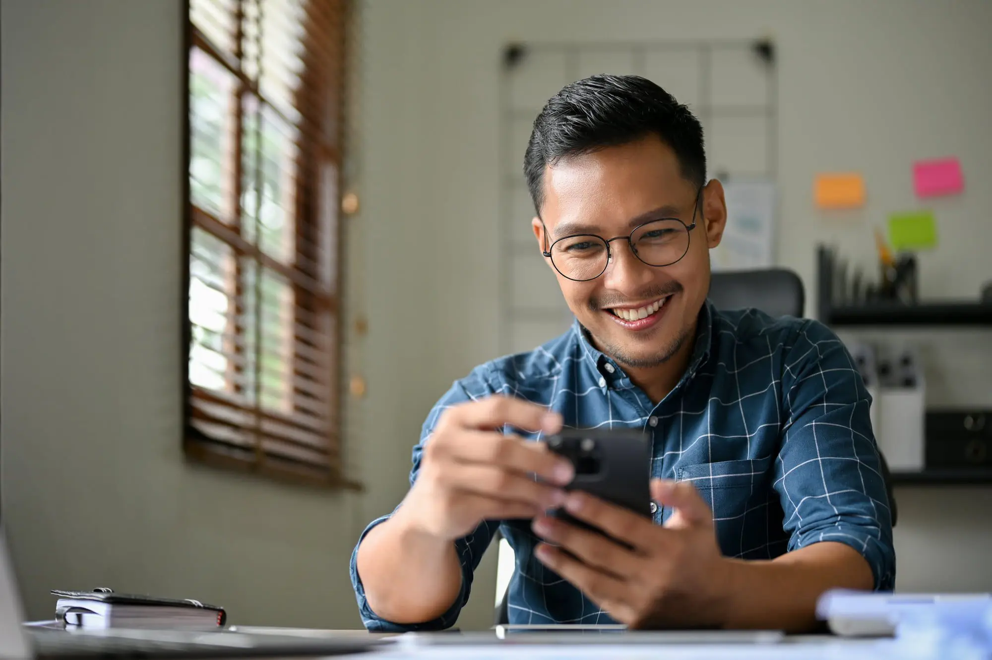 Emerald City Orthodontics Kirkland - Braces & Invisalign Smiling man in glasses and checkered shirt at desk, researching Braces Cost at Emerald City Orthodontics in Kirkland, WA.