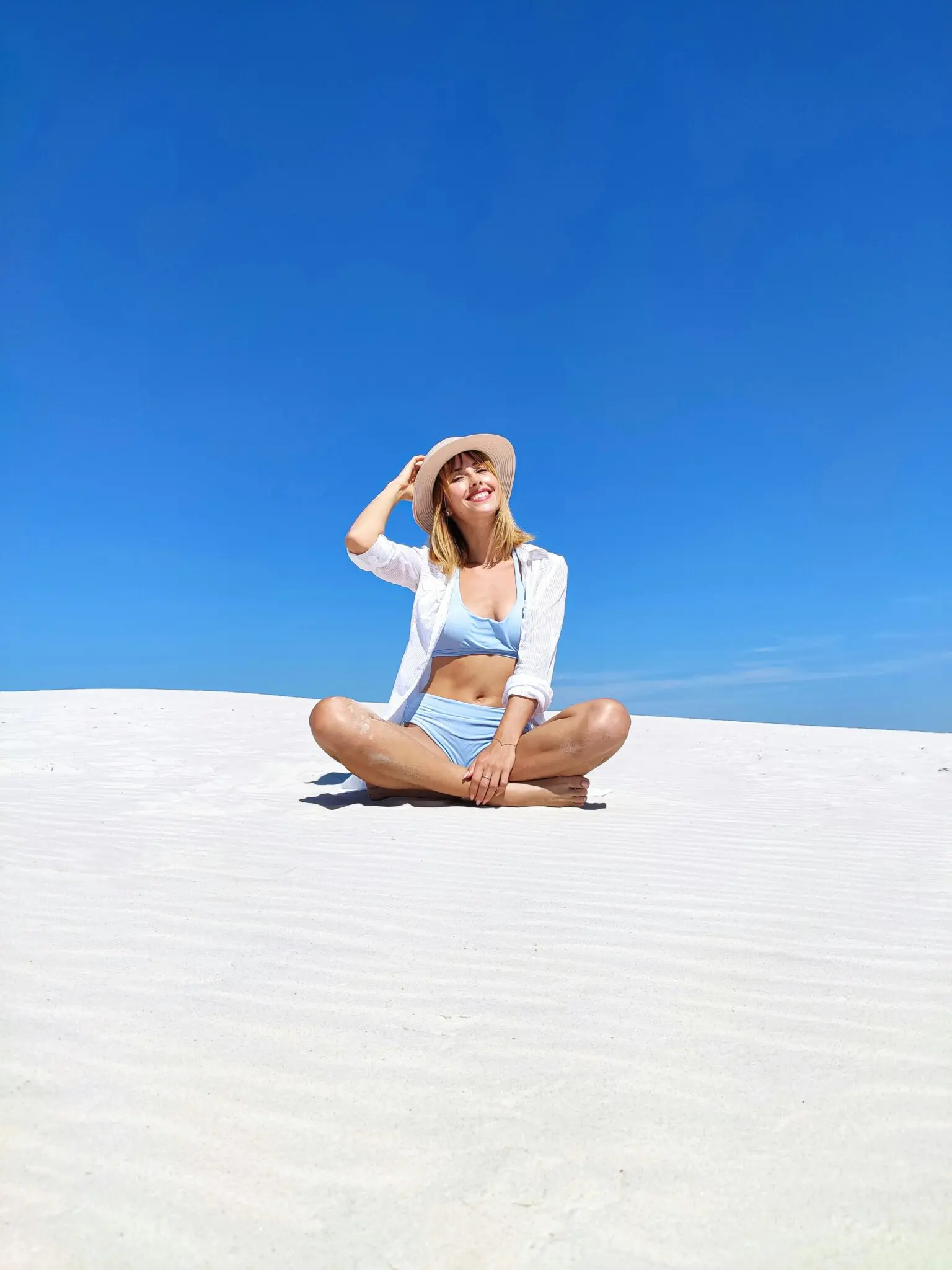 On white sand under a blue sky, a woman smiles and looks up, promoting prevention at Emerald City Orthodontics in Kirkland, WA.