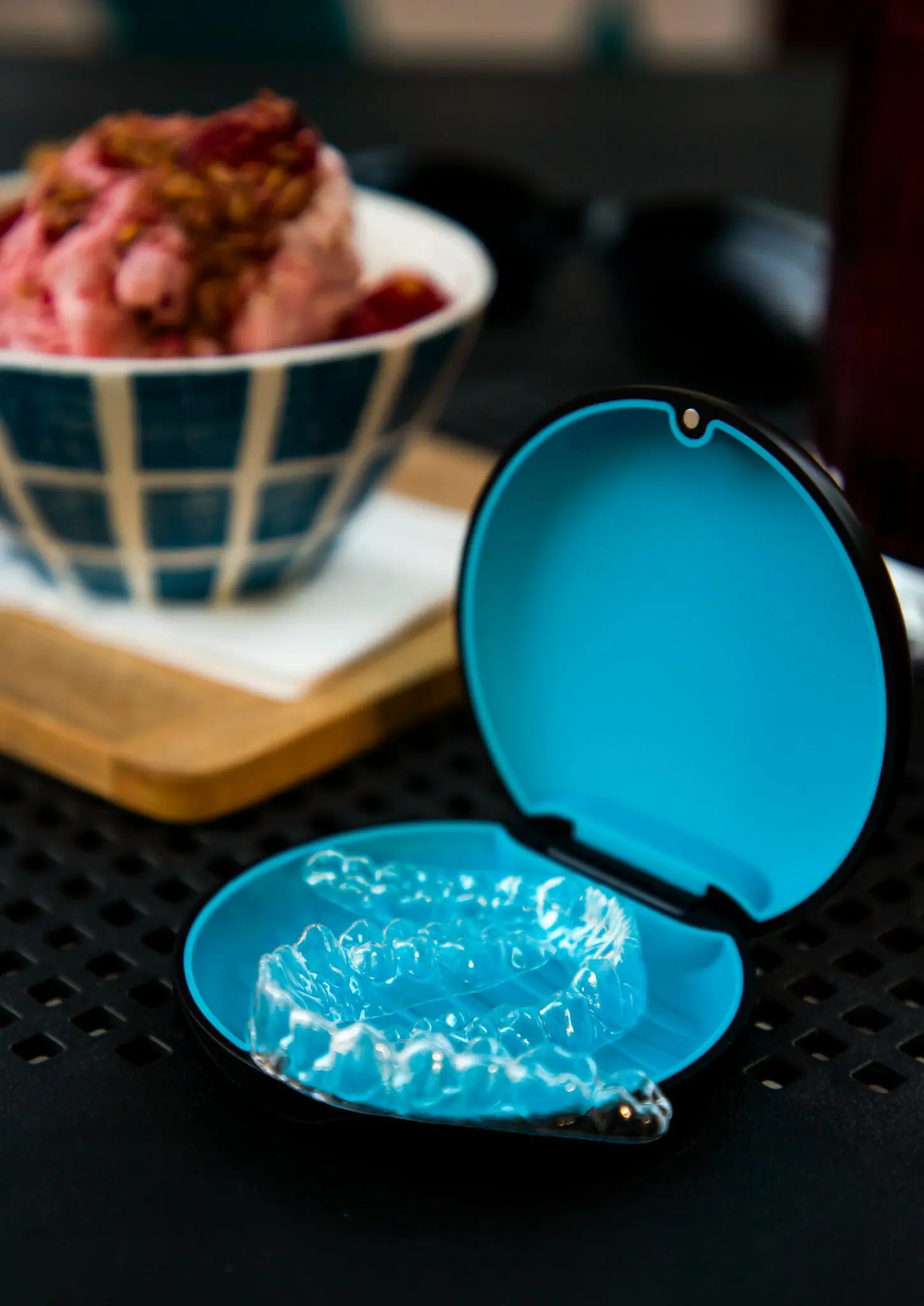 Clear dental aligners in a blue case sit on black near pink ice cream; Emerald City Orthodontics in Kirkland, WA can help check Invisalign Insurance.