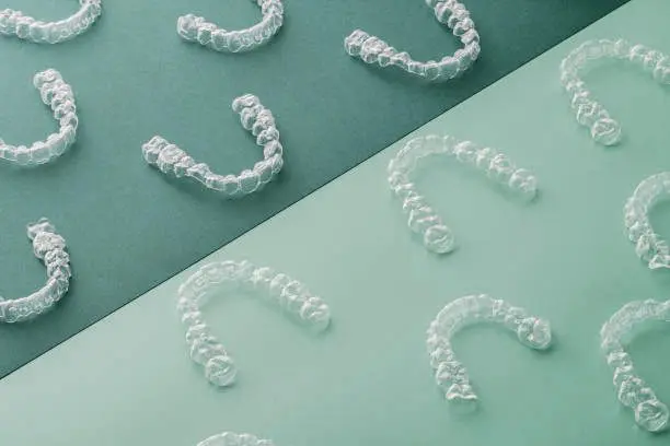 Invisalign® Clear Aligners in rows on green and turquoise, at Emerald City Orthodontics in Kirkland WA, viewed from above.