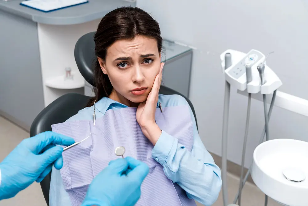 At Emerald City Orthodontics in Kirkland, WA, a worried woman holds her cheek in the dental chair as TMJ treatment is prepared - TMJ Treatment in Kirkland, WA