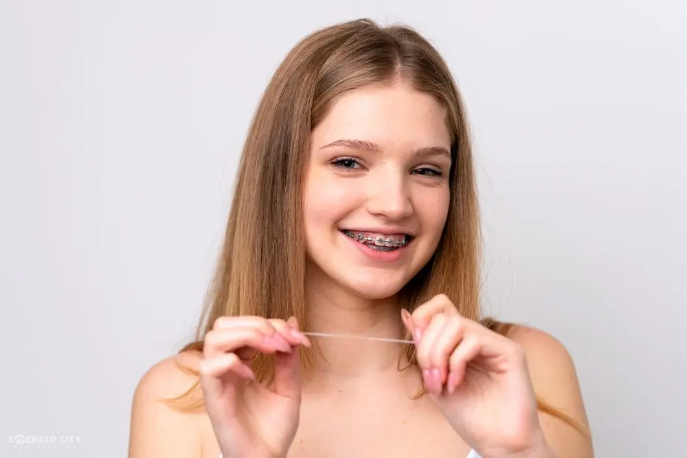 Smiling teen with braces demonstrates flossing technique, promoting Emerald City Orthodontics in Kirkland, WA, on white background - How to Floss with Braces in Kirkland, WA