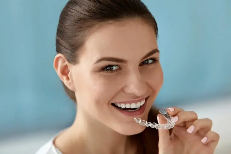 At Emerald City Orthodontics in Kirkland, WA, a woman smiles while holding an Invisalign aligner near her mouth - Can Invisalign Fix Overbite in Kirkland, WA