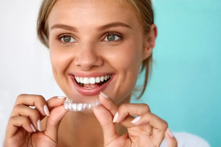 At Emerald City Orthodontics in Kirkland, WA, a woman smiles as she prepares to insert an Invisalign aligner into her mouth - How Does Invisalign Work in Kirkland, WA